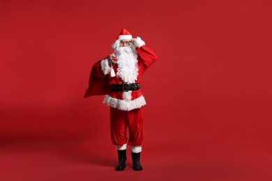 Photo of Santa Claus with bag of Christmas presents posing on red background