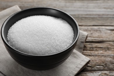 Photo of Granulated sugar in bowl on wooden table, closeup. Space for text