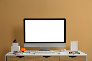 Photo of Stylish workplace with computer and stationery on wooden table near beige wall