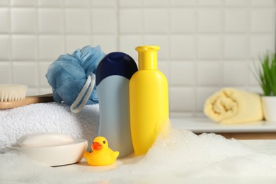 Baby cosmetic products, bath duck, brush and towel on white table. Space for text