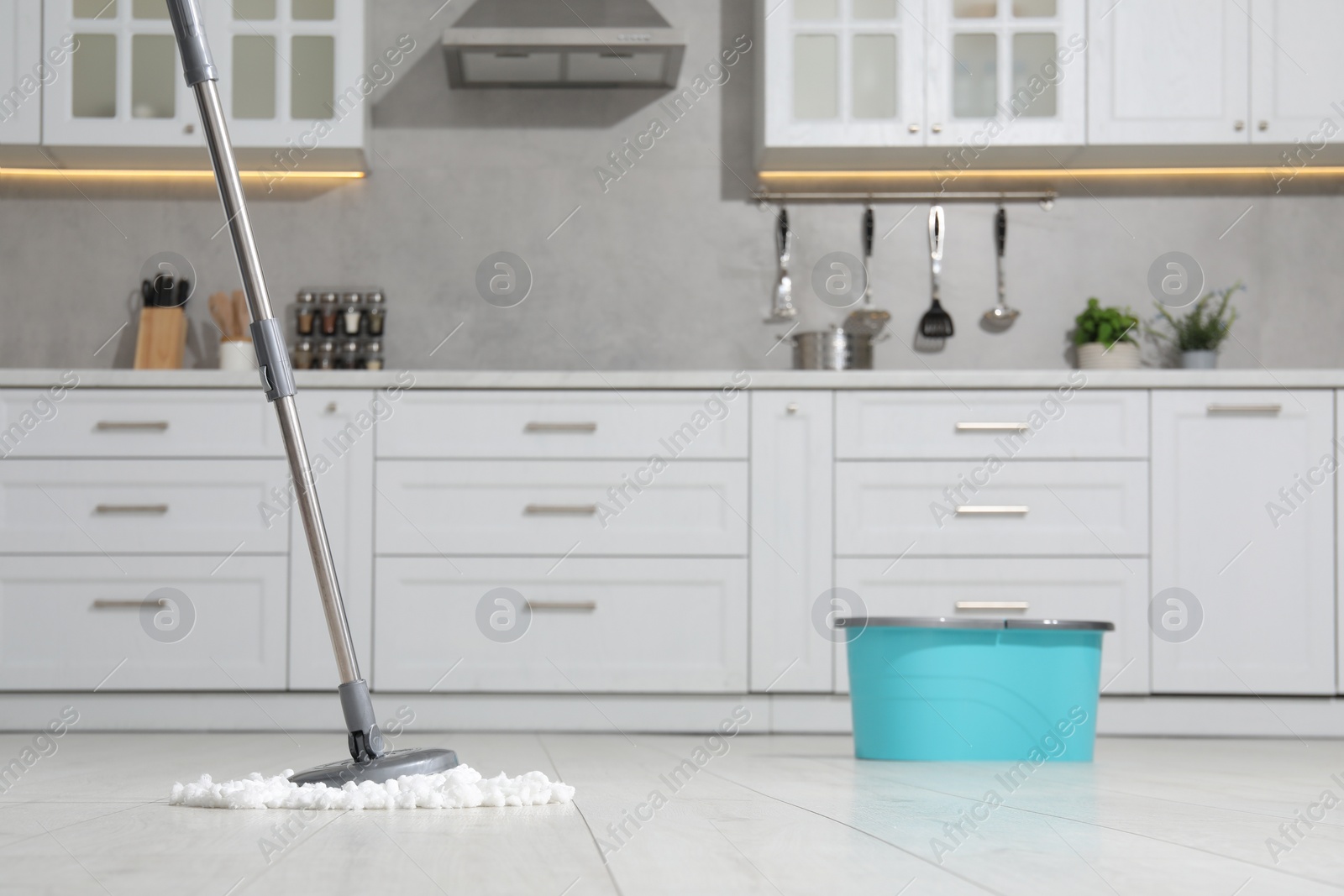 Photo of Mop and bucket on white parquet in kitchen. Cleaning floor