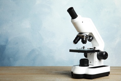 Modern microscope on wooden table against blue background, space for text. Medical equipment