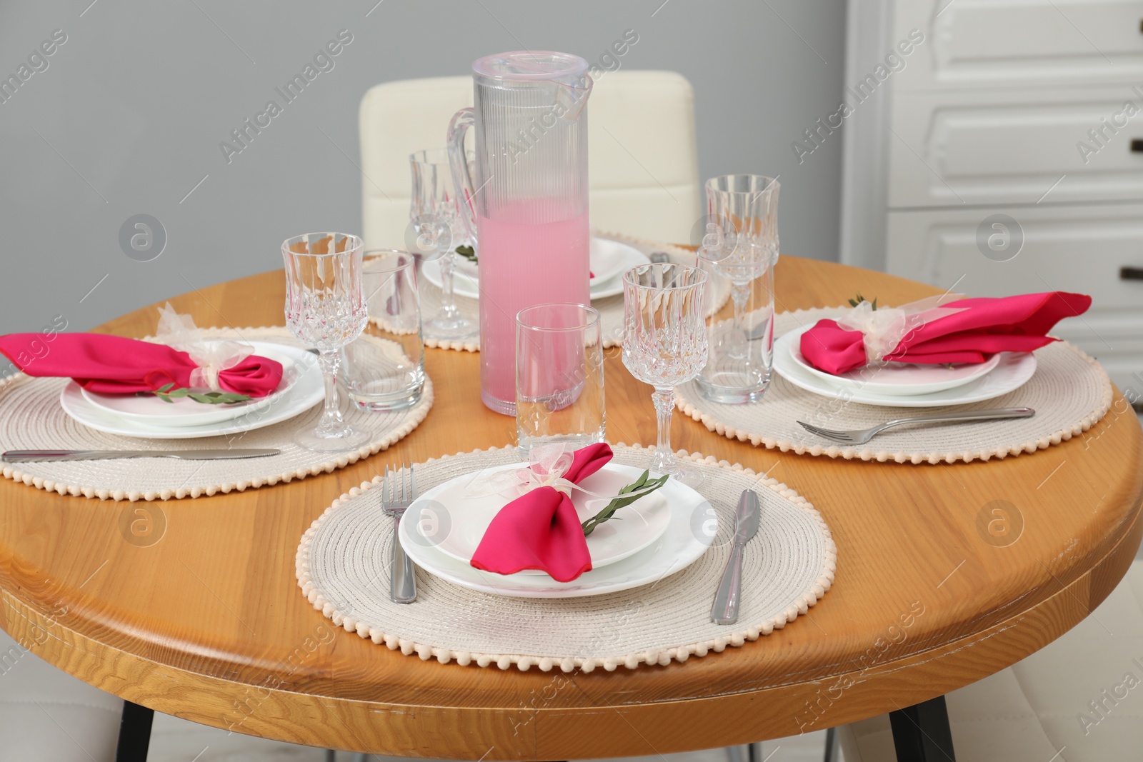 Photo of Color accent table setting. Glasses, plates, jug of beverage and pink napkins in dining room