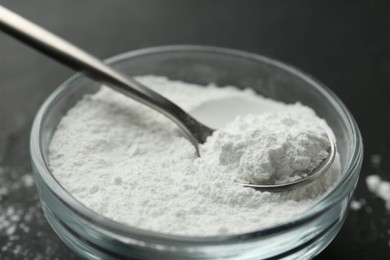 Photo of Baking powder in bowl and spoon on black table, closeup