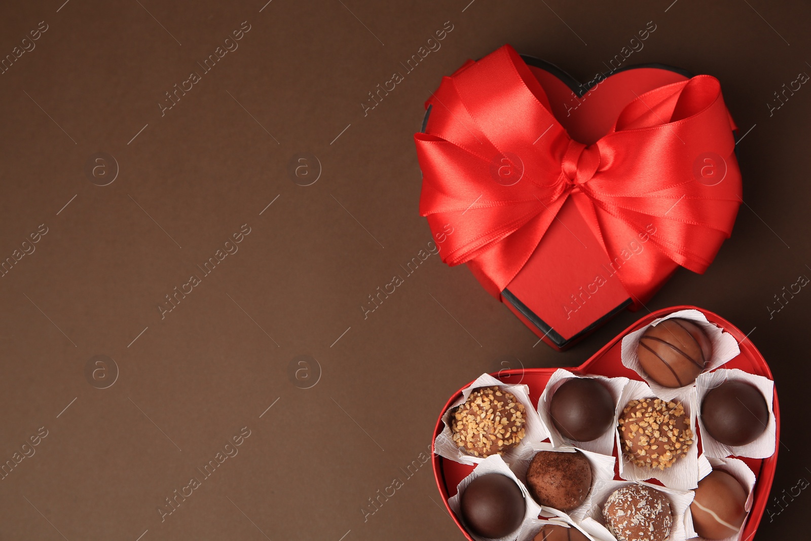 Photo of Heart shaped box with delicious chocolate candies on brown background, flat lay. Space for text