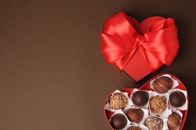 Photo of Heart shaped box with delicious chocolate candies on brown background, flat lay. Space for text