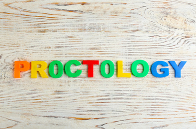 Photo of Word PROCTOLOGY made of colorful letters on white wooden table, flat lay. Hemorrhoid problems