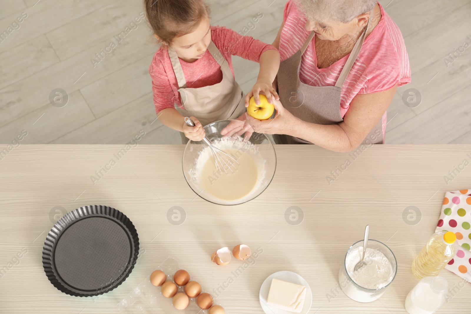 Photo of Little girl and her grandmother cooking at table with products, top view