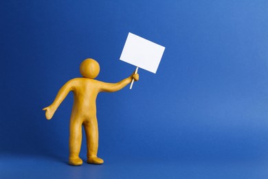 Photo of Human figure made of yellow plasticine holding blank sign on blue background. Space for text