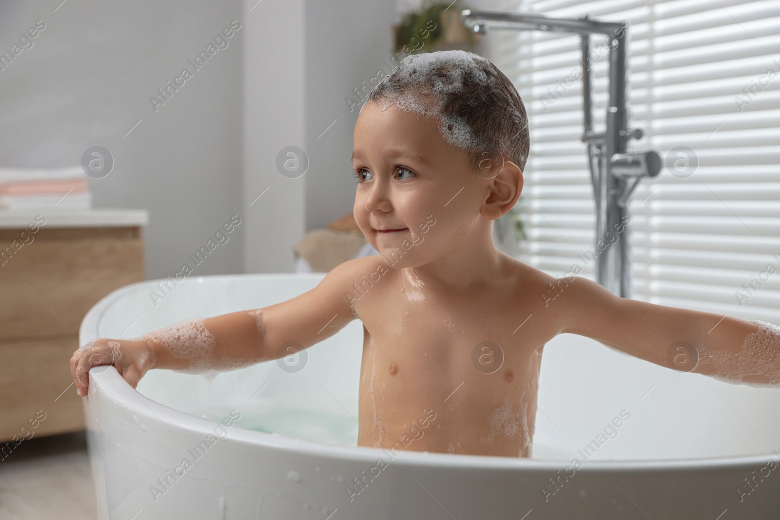 Photo of Cute little boy washing hair with shampoo in bathroom