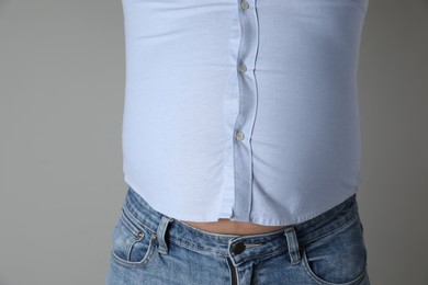 Photo of Overweight man in tight shirt on grey background, closeup