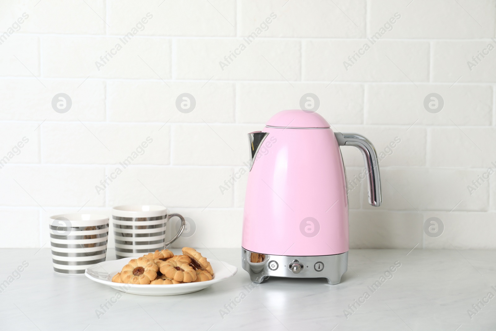 Photo of Modern electric kettle, cups and cookies on counter in kitchen