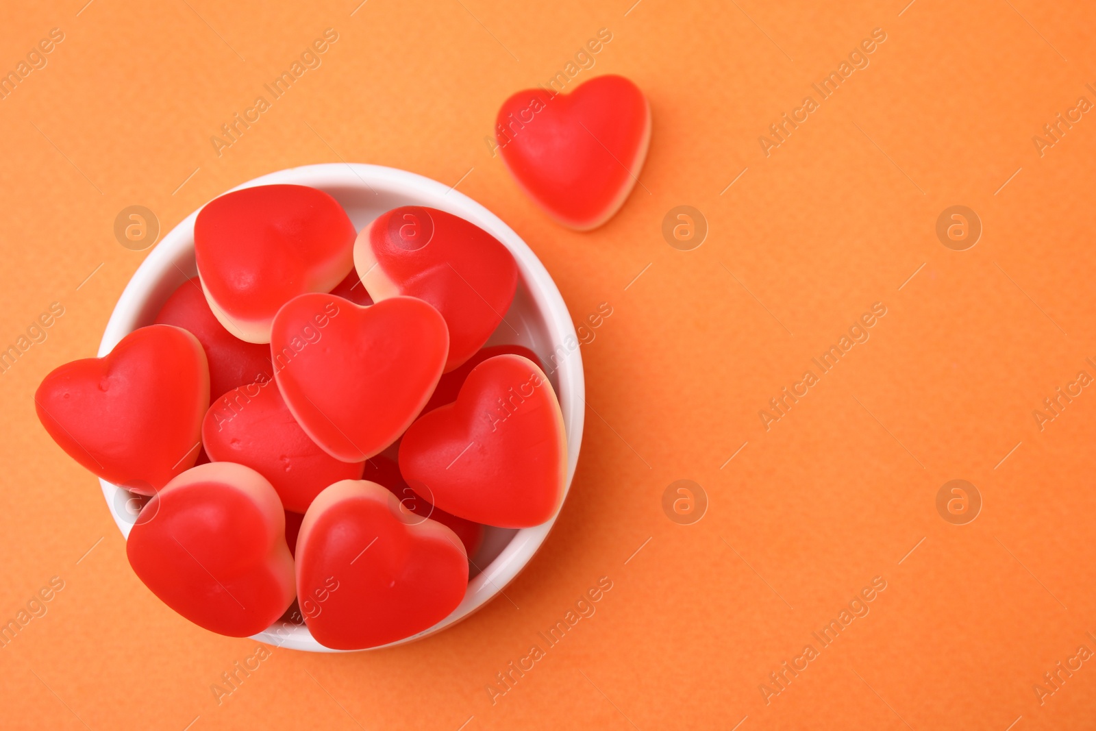 Photo of Bowl and delicious heart shaped jelly candies on orange background, flat lay. Space for text
