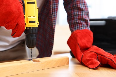 Young handyman working with electric drill at table in workshop, closeup