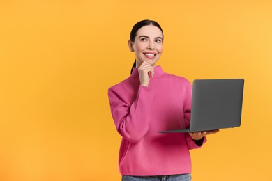 Photo of Thoughtful woman with laptop on orange background