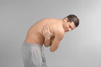 Young man suffering from back pain on grey background