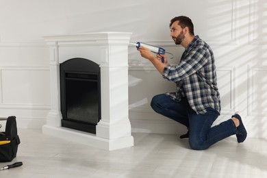 Photo of Man sealing electric fireplace with caulk near white wall in room