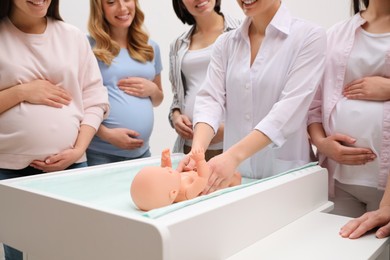 Photo of Pregnant women learning how to swaddle baby at courses for expectant mothers indoors, closeup