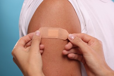 Photo of Nurse sticking plaster on man's arm after vaccination against light blue background, closeup