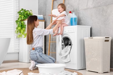 Mother with her daughter having fun while washing baby clothes in bathroom