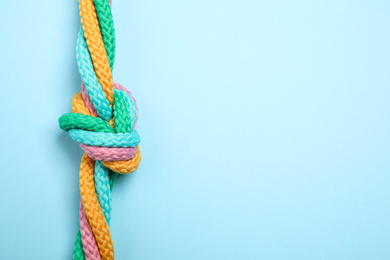 Photo of Top view of colorful ropes tied together on light blue background, space for text. Unity concept