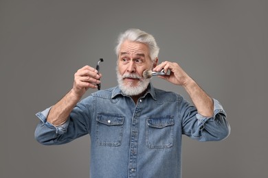 Photo of Senior man with mustache holding razor and brush on grey background