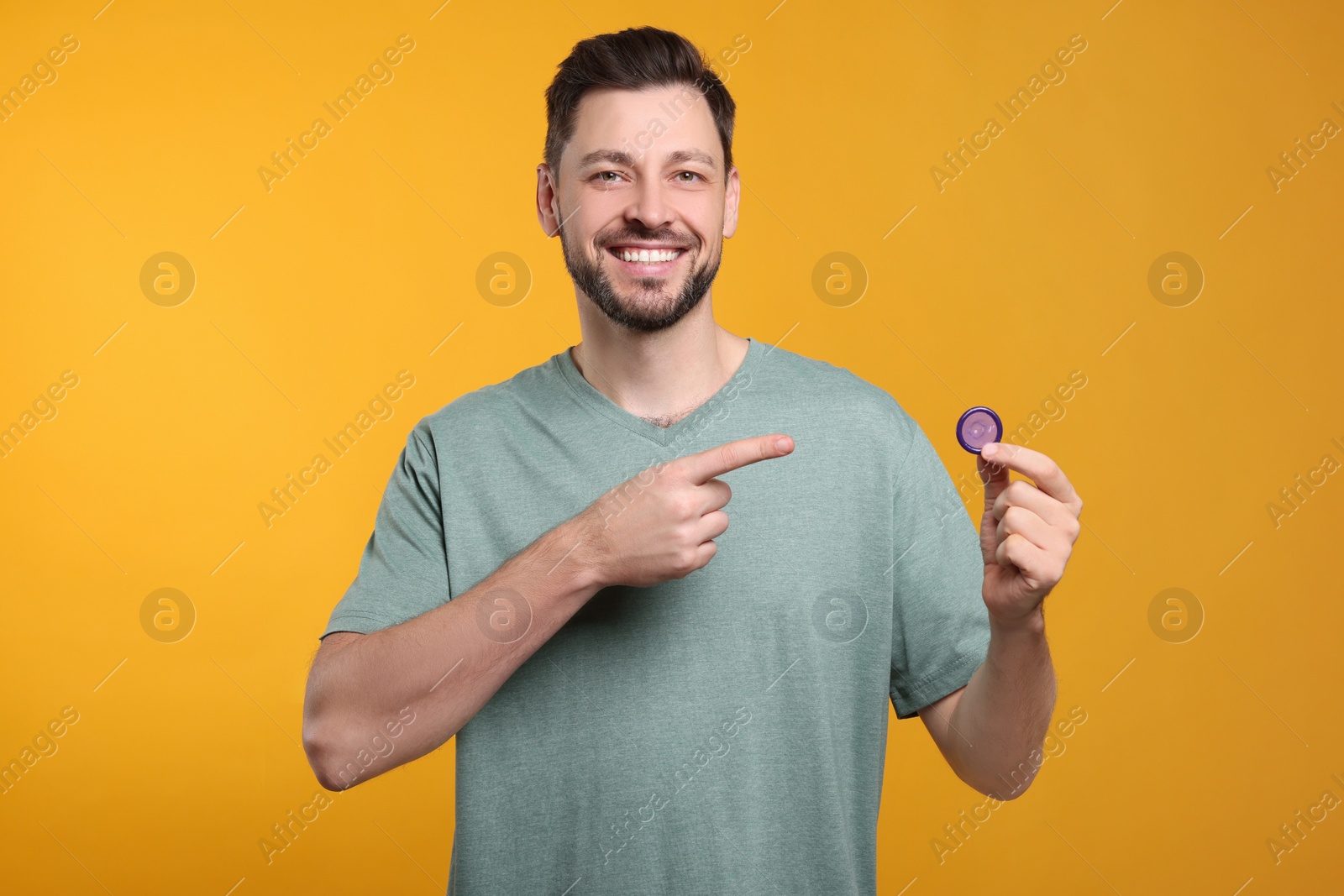 Photo of Happy man holding condom on orange background