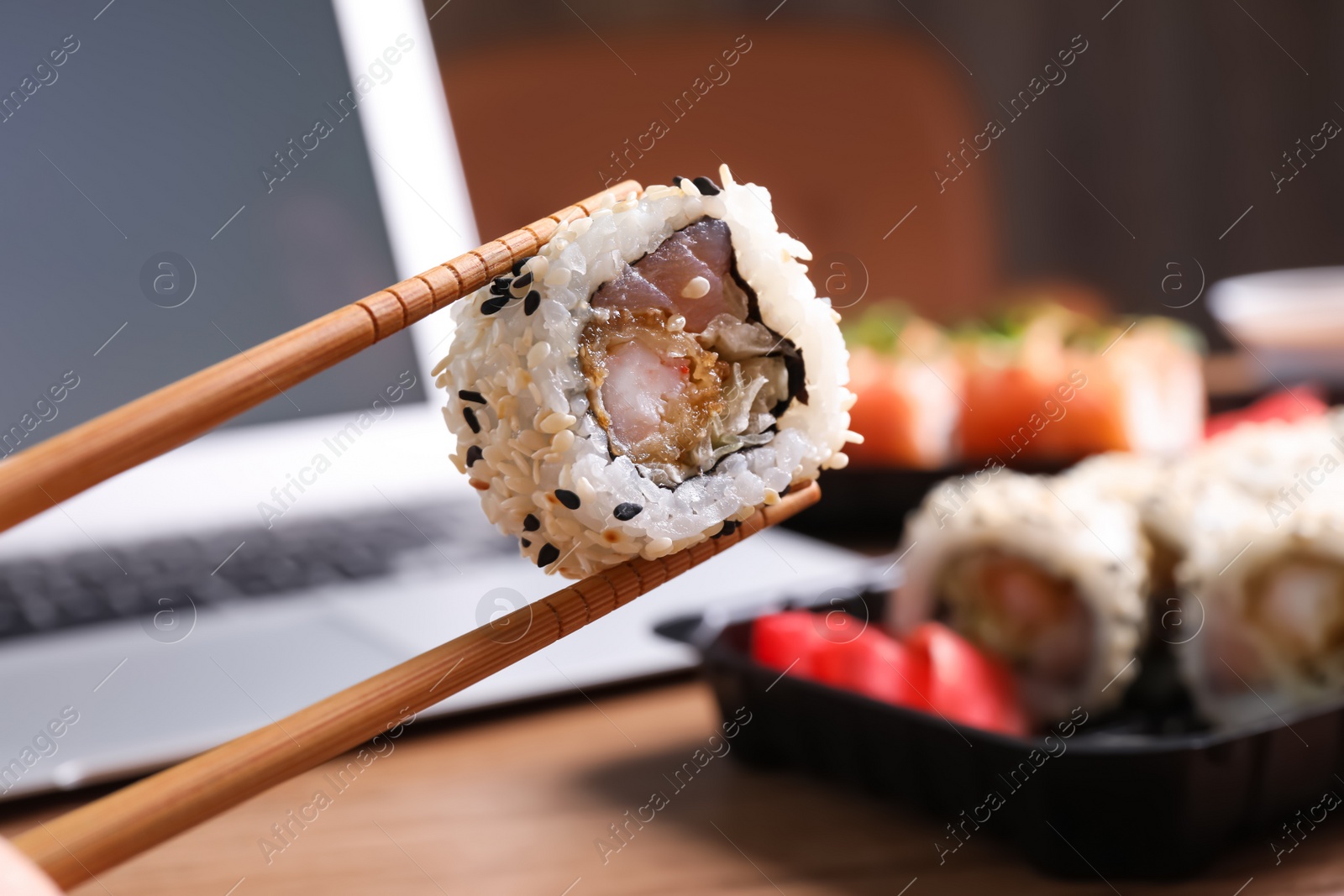 Photo of Holding sushi roll with chopsticks over table, closeup