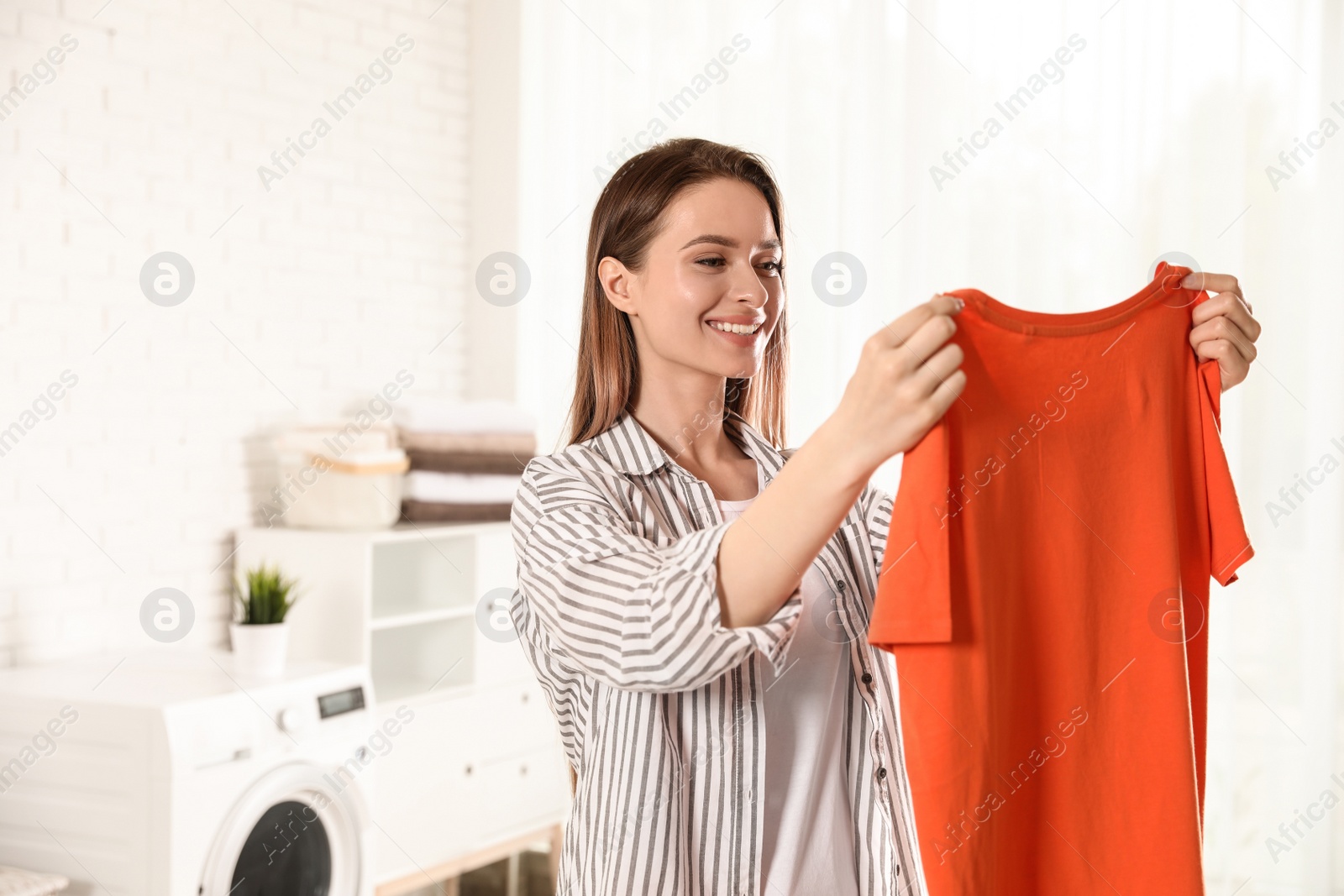 Photo of Happy young woman with clean t-shirt indoors. Laundry day