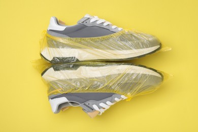 Photo of Sneakers in shoe covers on yellow background, top view