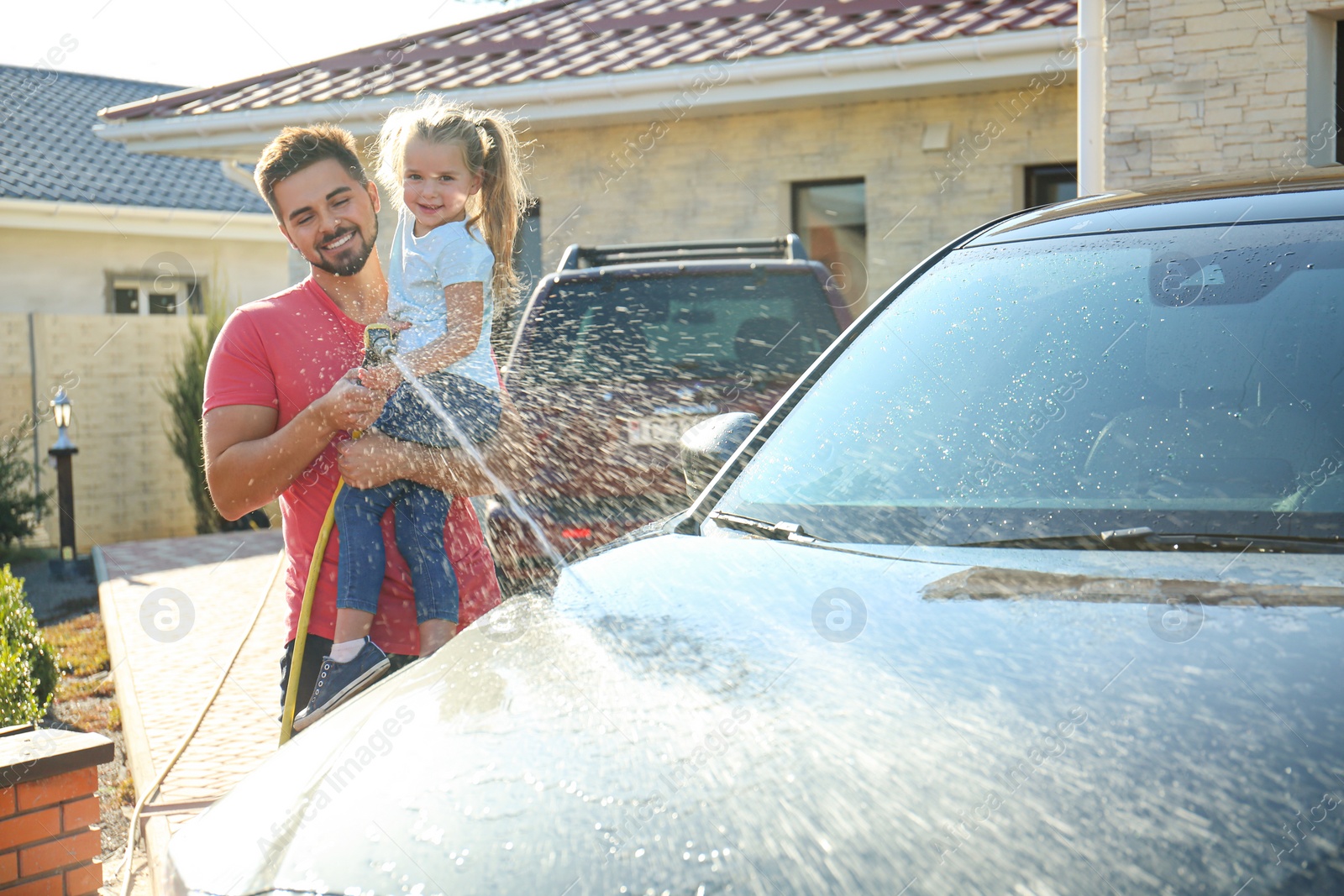 Photo of Dad and daughter washing car at backyard on sunny day