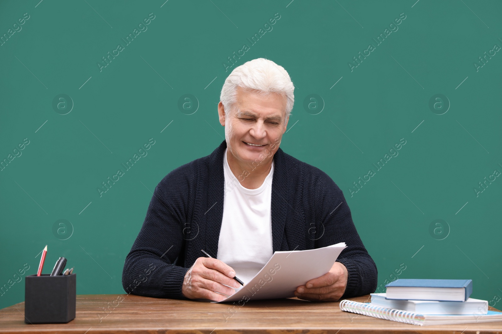 Photo of Portrait of senior teacher at table against green chalkboard