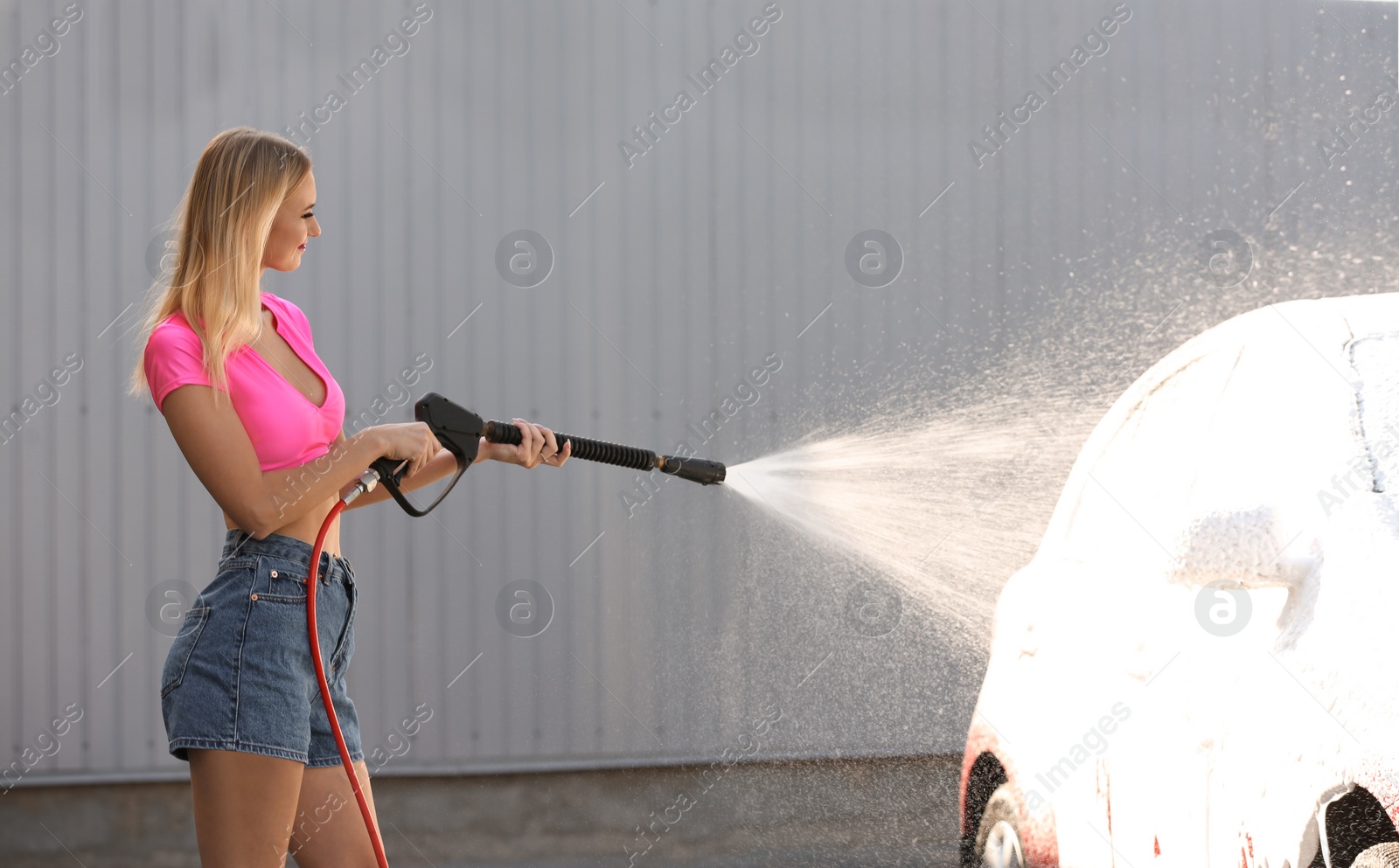 Photo of Young woman cleaning automobile with high pressure water jet at car wash