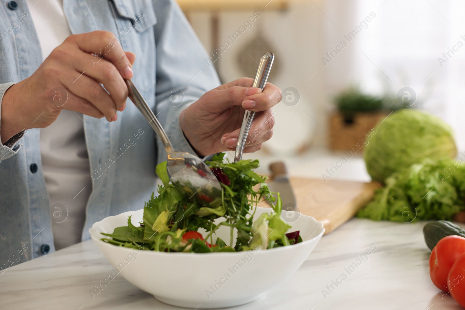 Photo of Woman making salad at white marble table in kitchen, closeup