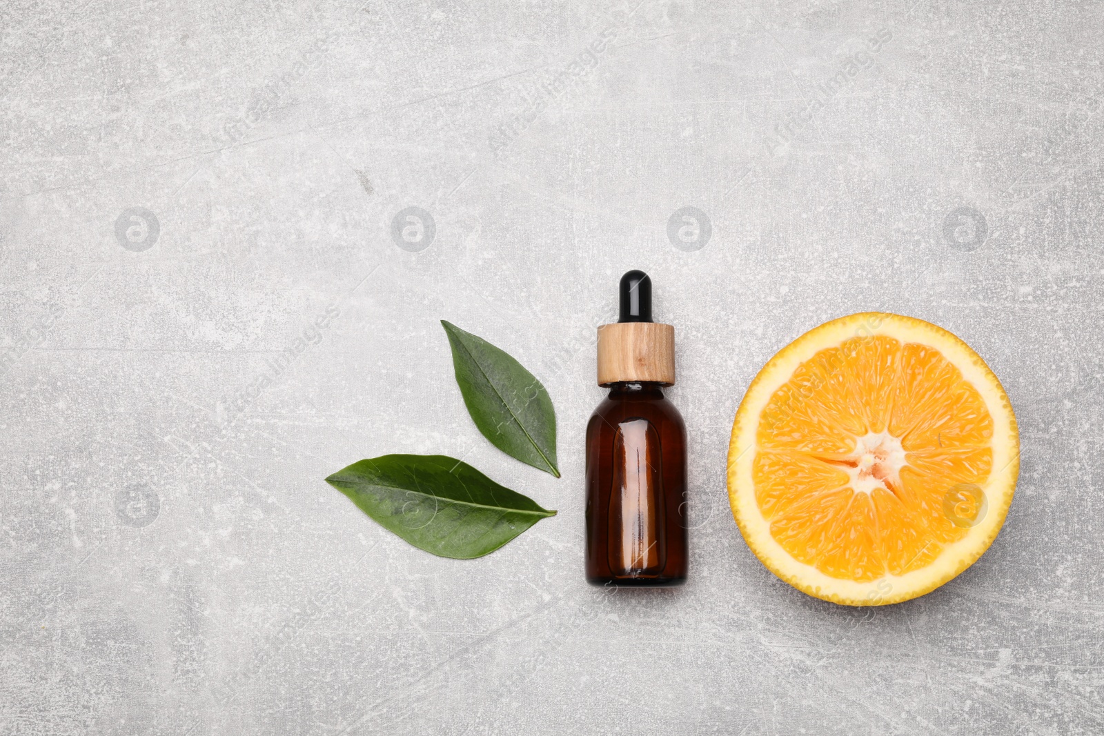 Photo of Bottle of essential oil with orange slice and leaves on grey stone table, flat lay