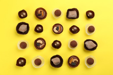 Different delicious chocolate candies on yellow background, flat lay