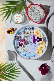 Photo of Delicious smoothie bowl with fresh fruits, blueberries and flowers served on textured table, flat lay