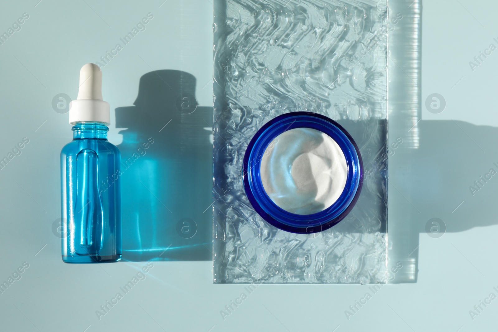 Photo of Bottle and jar of cosmetic products on light blue background, flat lay