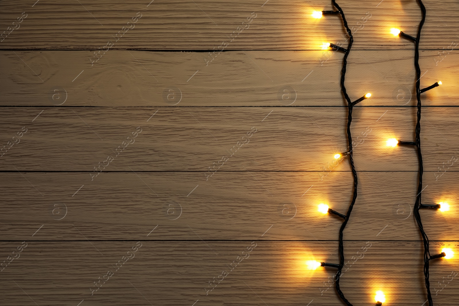 Photo of Glowing festive lights on wooden background, top view. Space for text