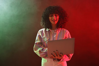 Beautiful young woman with laptop on color background in neon lights