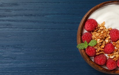 Photo of Bowl of tasty yogurt with raspberries and muesli served on blue wooden table, top view. Space for text