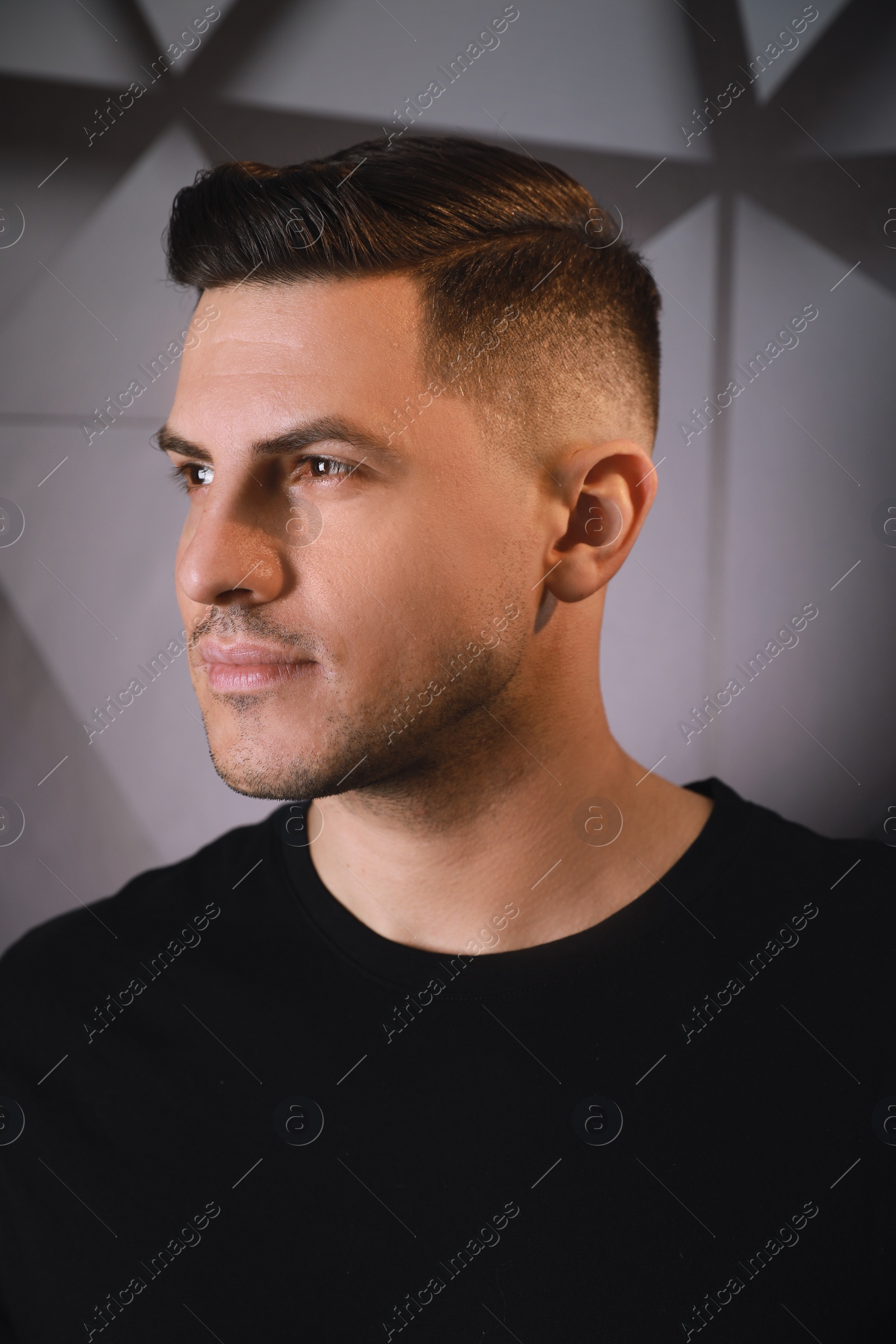 Photo of Handsome man with trendy hairstyle near dark wall