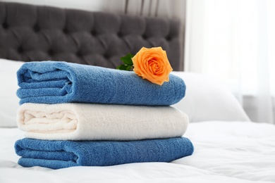 Stack of clean towels and beautiful rose flower on bed. Space for text