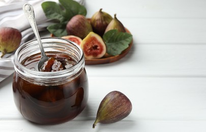 Photo of Jar of tasty sweet jam and fresh figs on white wooden table. Space for text