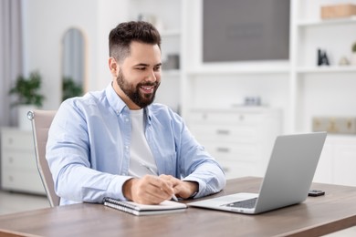 Photo of Young man watching webinar at table in room