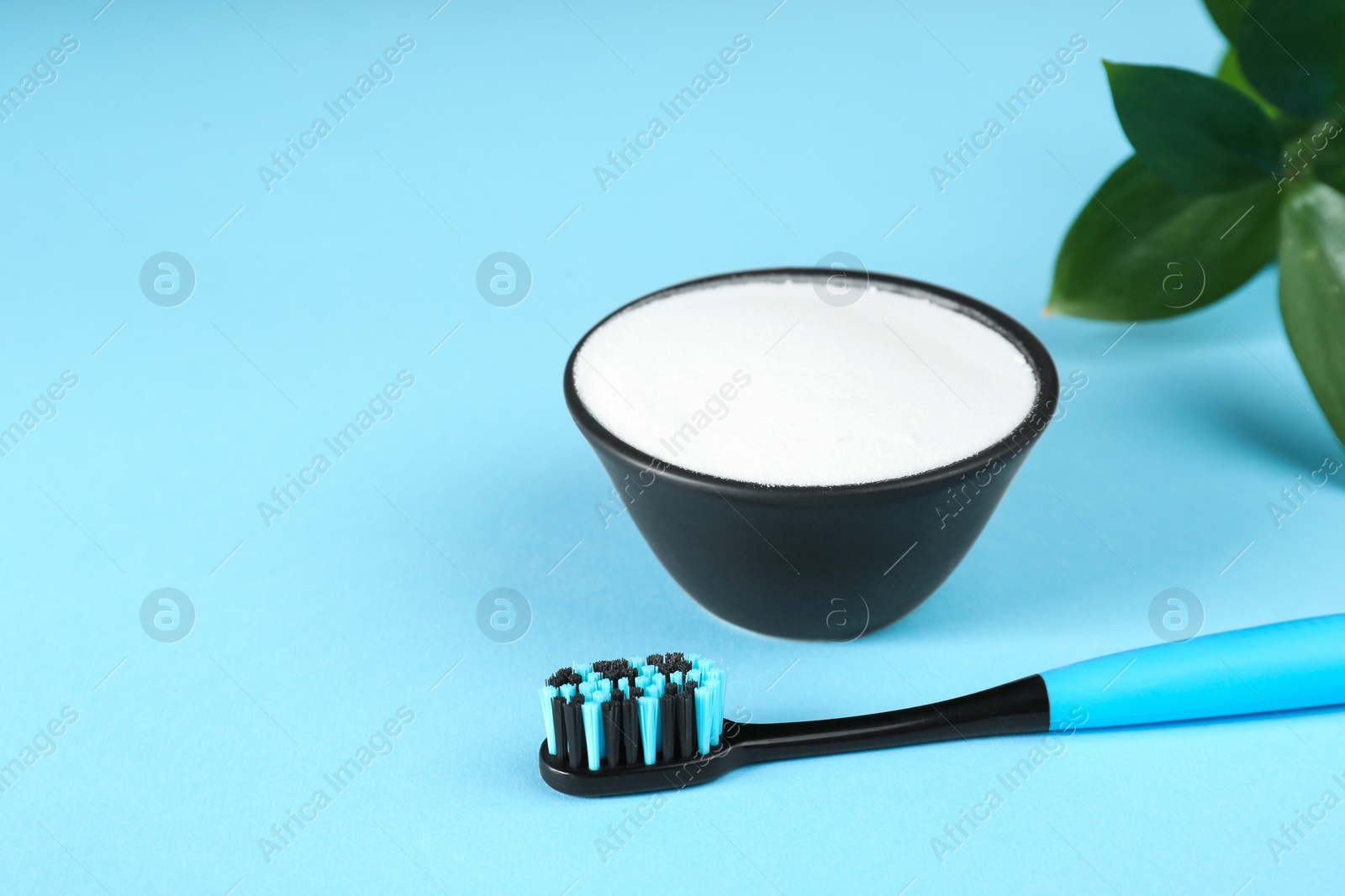 Photo of Toothbrush and bowl with baking soda on light blue background. Space for text