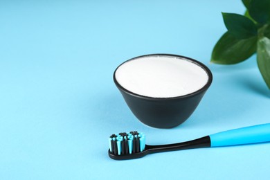 Photo of Toothbrush and bowl with baking soda on light blue background. Space for text