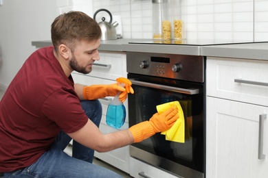 Photo of Young man cleaning oven with rag in kitchen