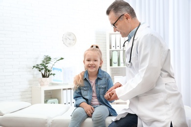 Doctor checking little girl's pulse with fingers in hospital. Space for text