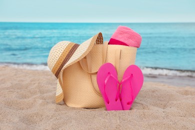 Summer bag with slippers, beach towel and straw hat on sand near sea